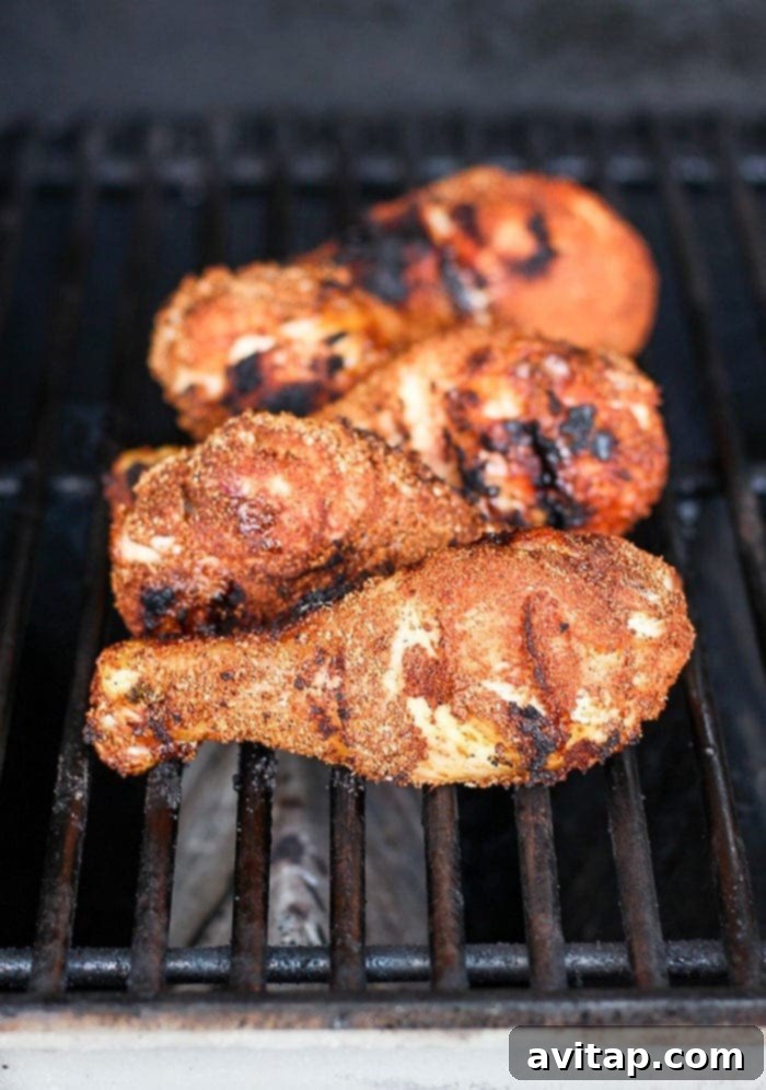 Crispy grilled chicken legs cooking over an open flame on a barbecue.