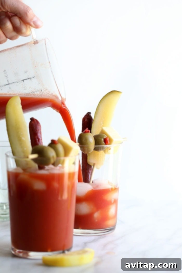 A hand pouring a rich red Bloody Mary mix into a tall glass filled with ice, setting the stage for garnishing.