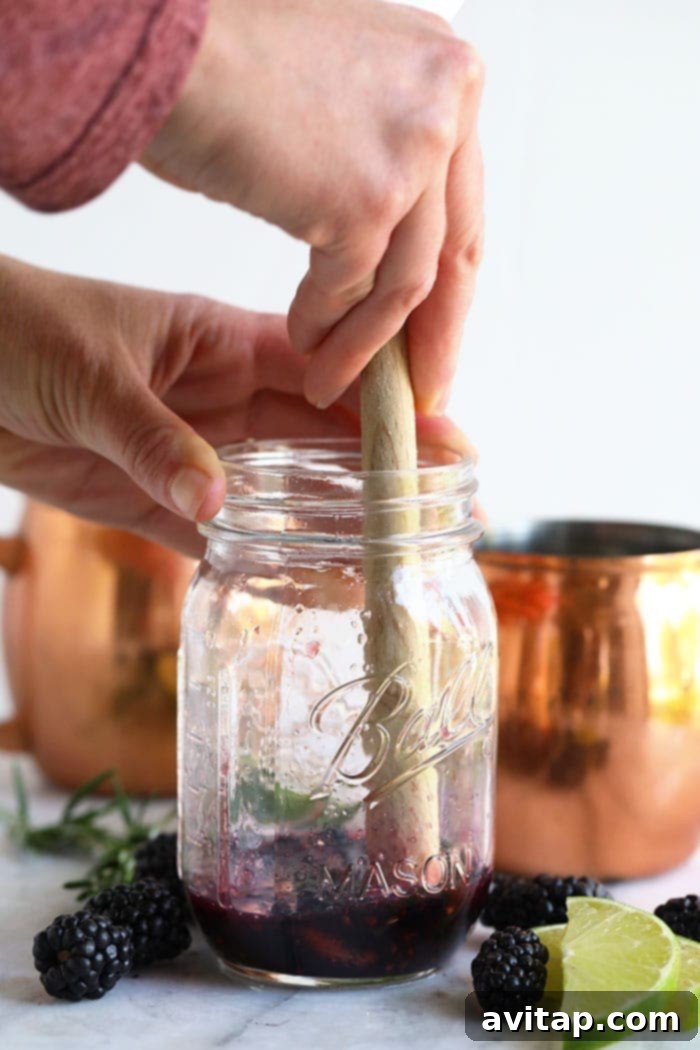Hand muddling fresh blackberries and mint in a cocktail shaker for a Moscow Mule