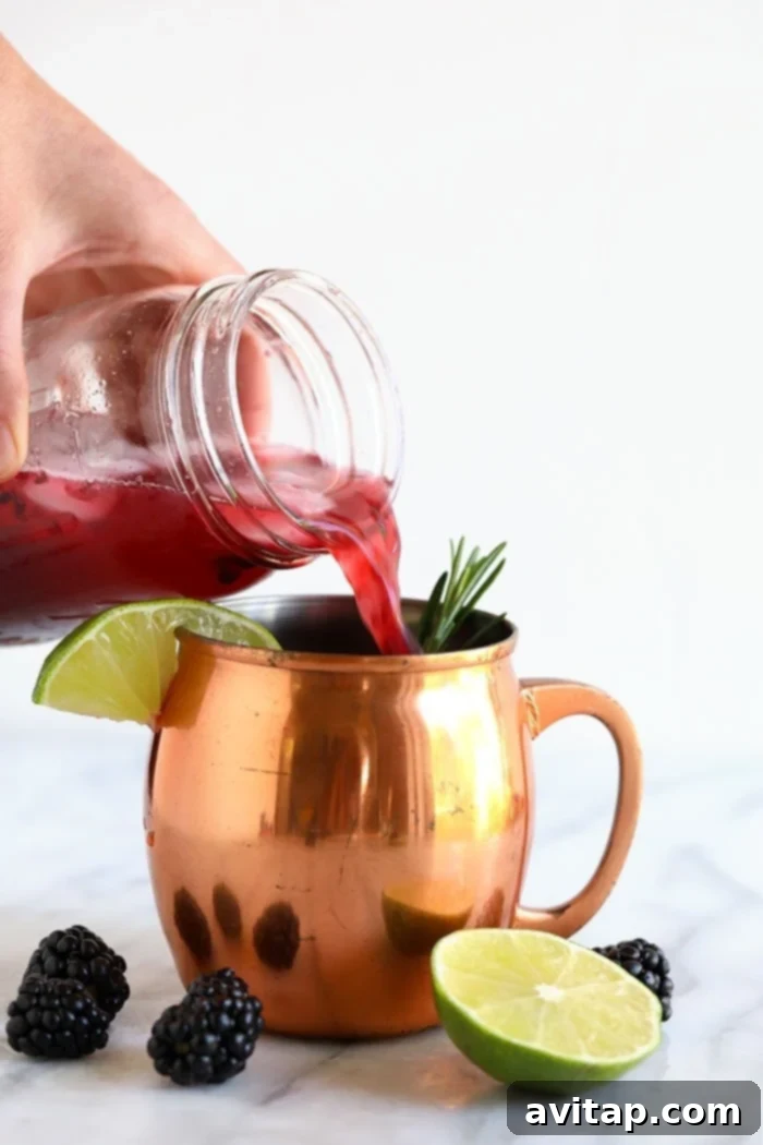 Pouring a freshly mixed Blackberry Moscow Mule into a copper mug filled with ice