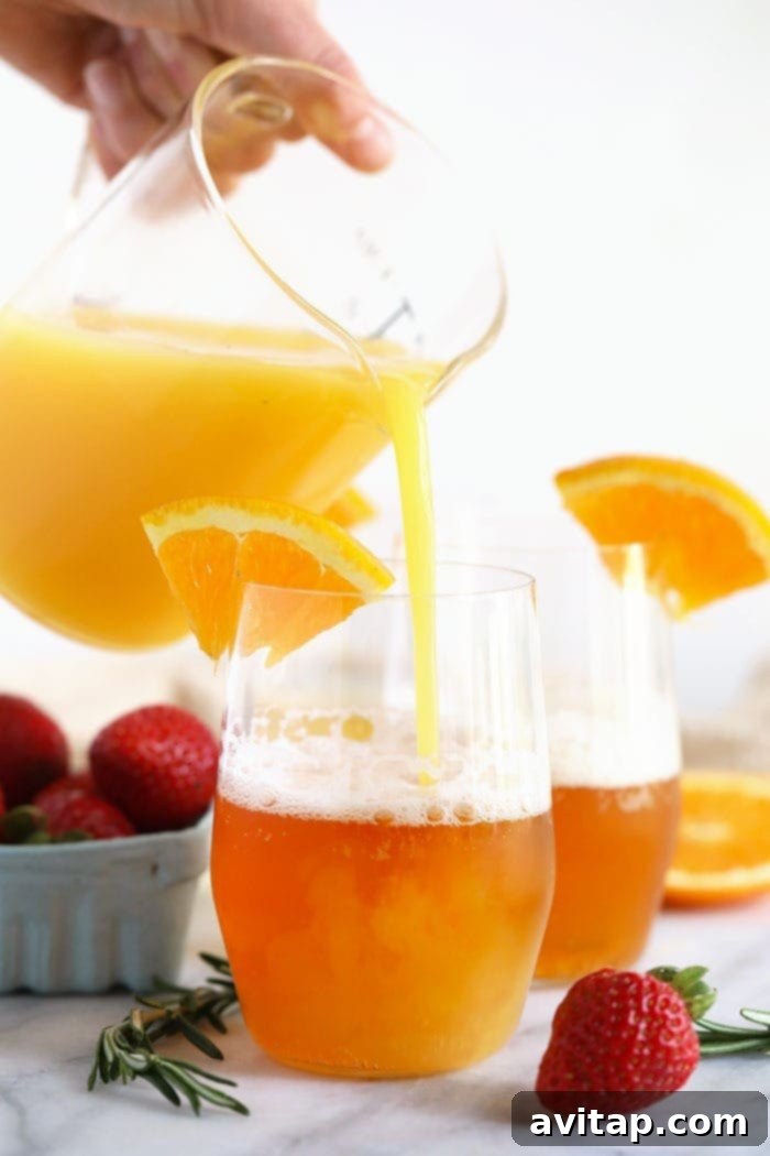 A hand carefully pouring fresh orange juice into a glass of light beer to create a vibrant Beermosa.