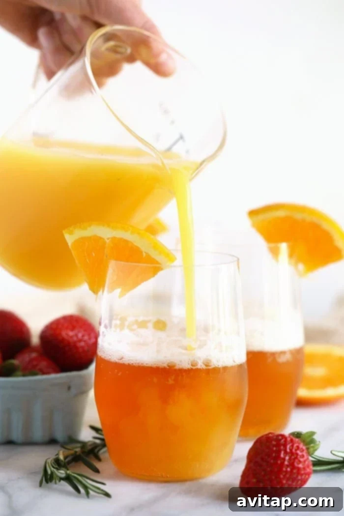 A hand pouring fresh orange juice into a glass of light beer to create a Beermosa, set on a bright table.