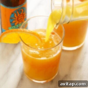 A glass of orange juice being poured into a Beermosa, creating a vibrant orange hue.