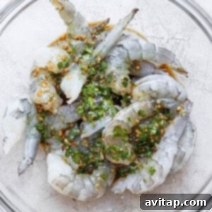 Shrimp marinating in a glass bowl with herbs and spices.