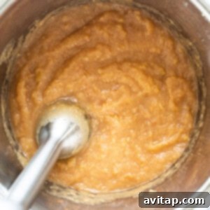An immersion blender mixing cooked apples in an Instant Pot to make applesauce.