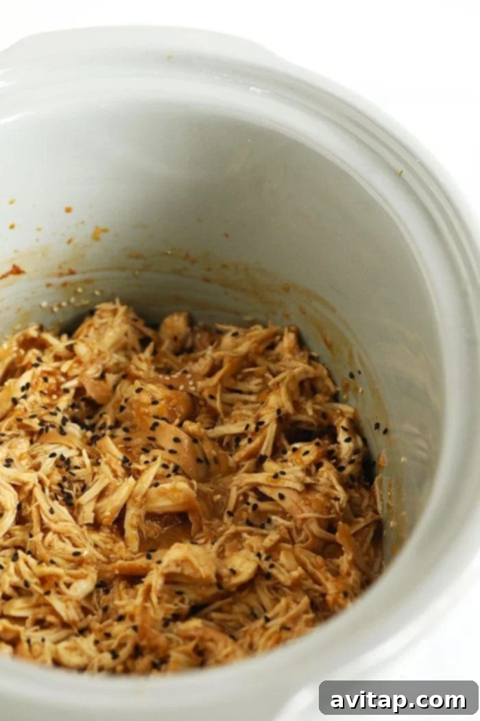 Perfectly Shredded Teriyaki Chicken from the Slow Cooker Shredded teriyaki chicken fully coated in sauce, simmering in a slow cooker.