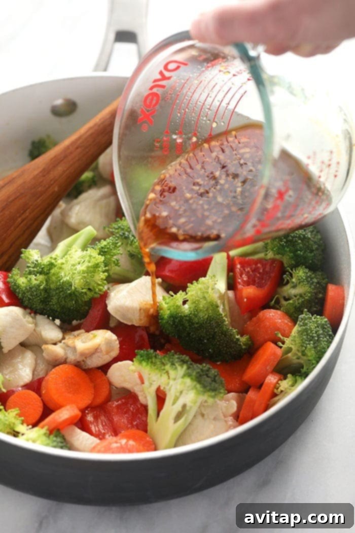 Pouring homemade teriyaki sauce over chicken and mixed vegetables in a pan