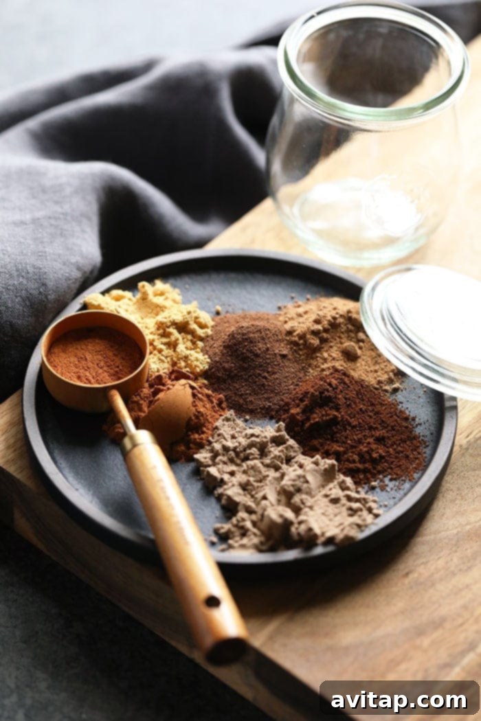 Various types of chai spices scattered on a dark plate, ready to be blended into a homemade mix.
