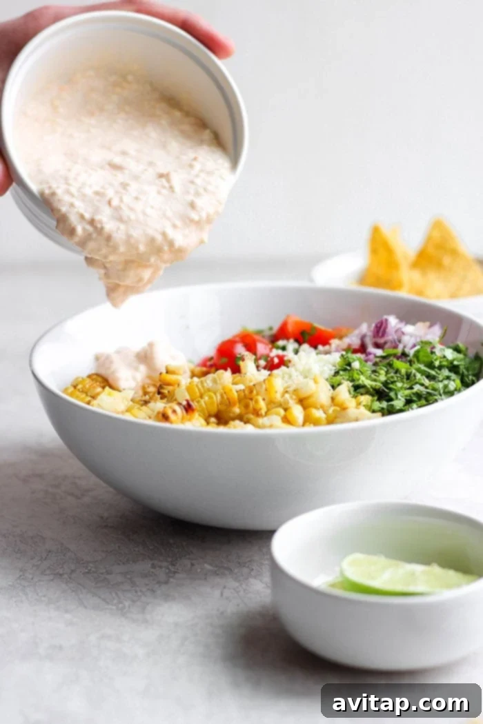 Pouring creamy cotija yogurt sauce over Mexican Street Corn Salad.