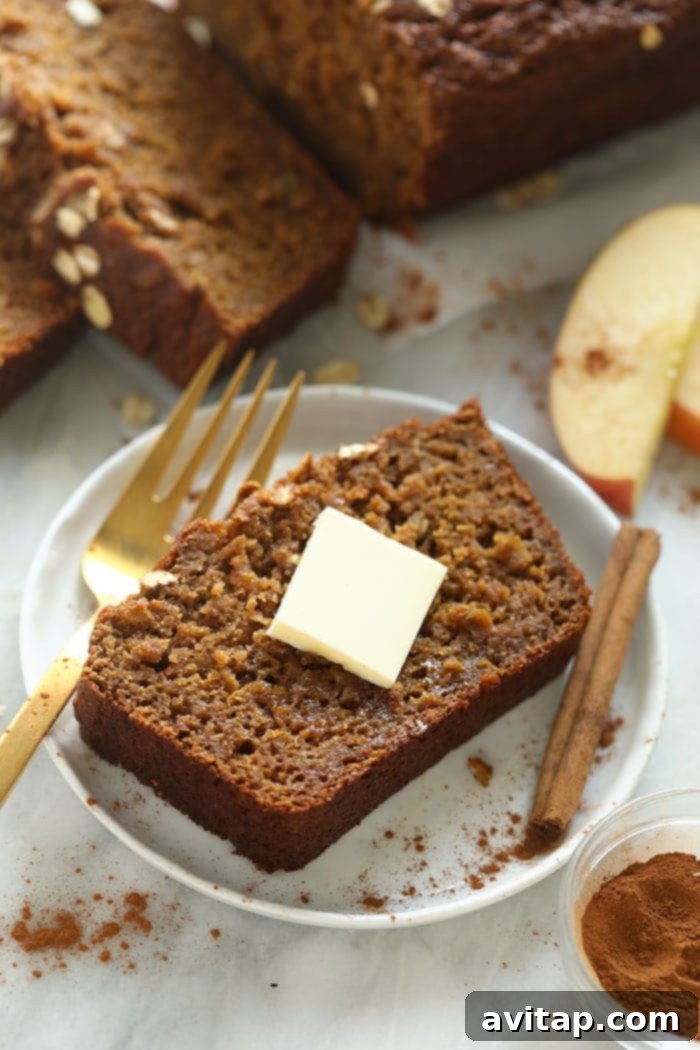 A thick slice of cinnamon apple bread on a plate, adorned with a pat of butter, inviting a delicious bite.