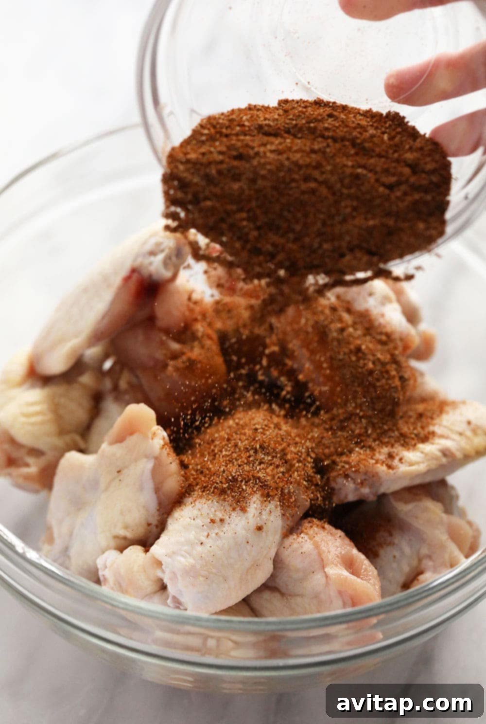 Seasoning Chicken Wings with Dry Rub Chef seasoning chicken wings generously with a rich homemade dry rub before baking.