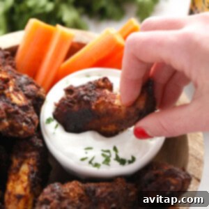 A person enjoying dry rub wings by dipping them into a bowl of dip.