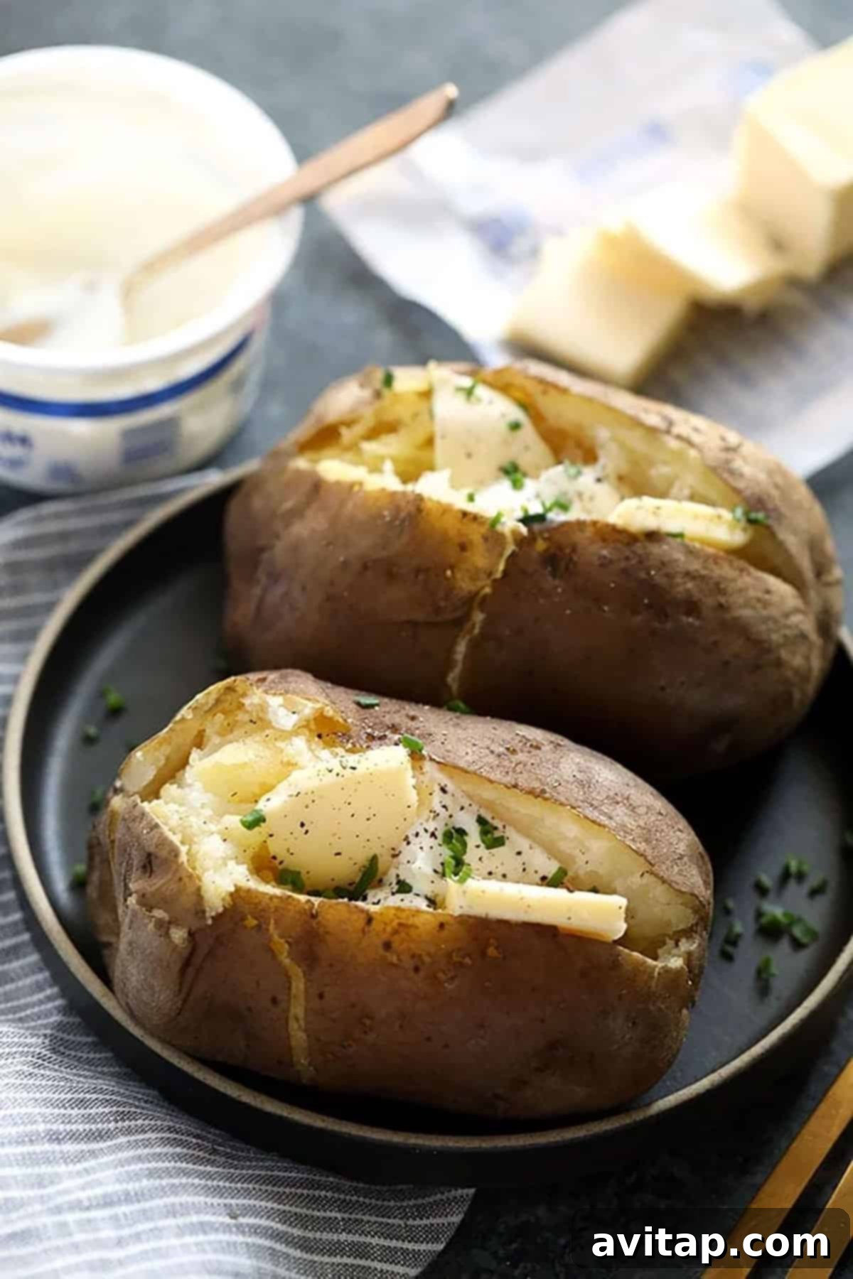 Two crock pot baked potatoes with melted cheese and fresh chives on a rustic plate, ready to be served.
