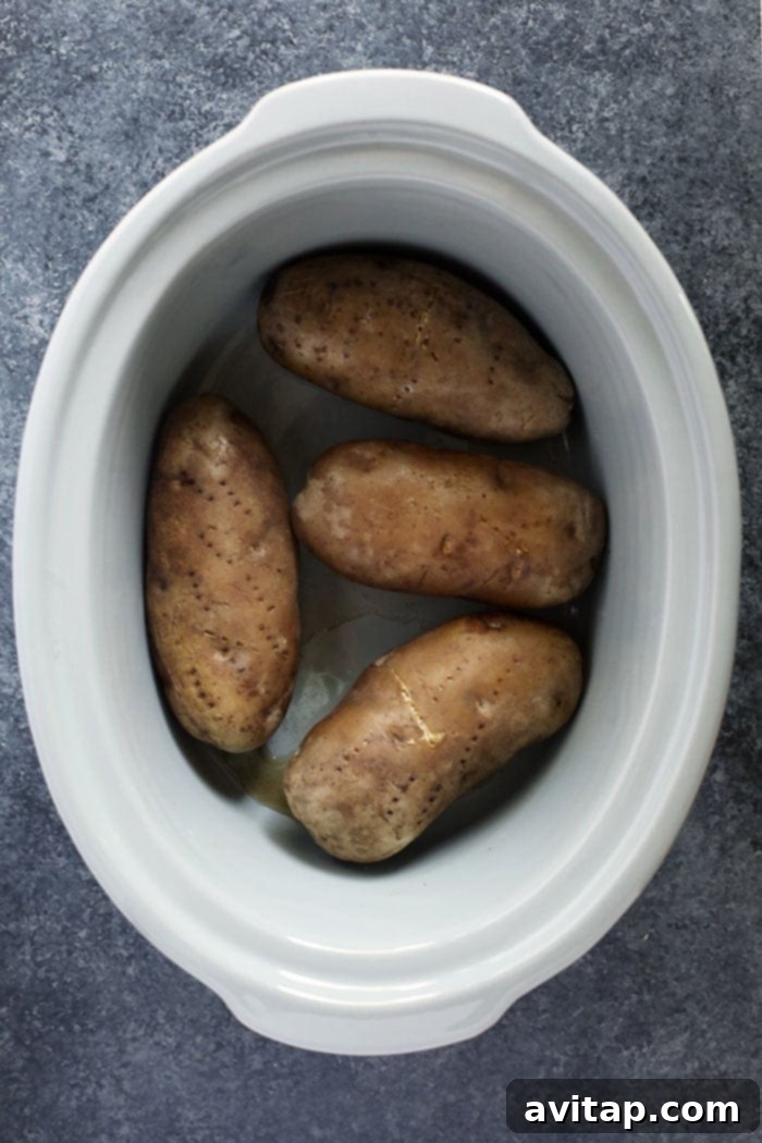 Multiple baked potatoes cooking inside a slow cooker, showing the steam and warmth of the process.