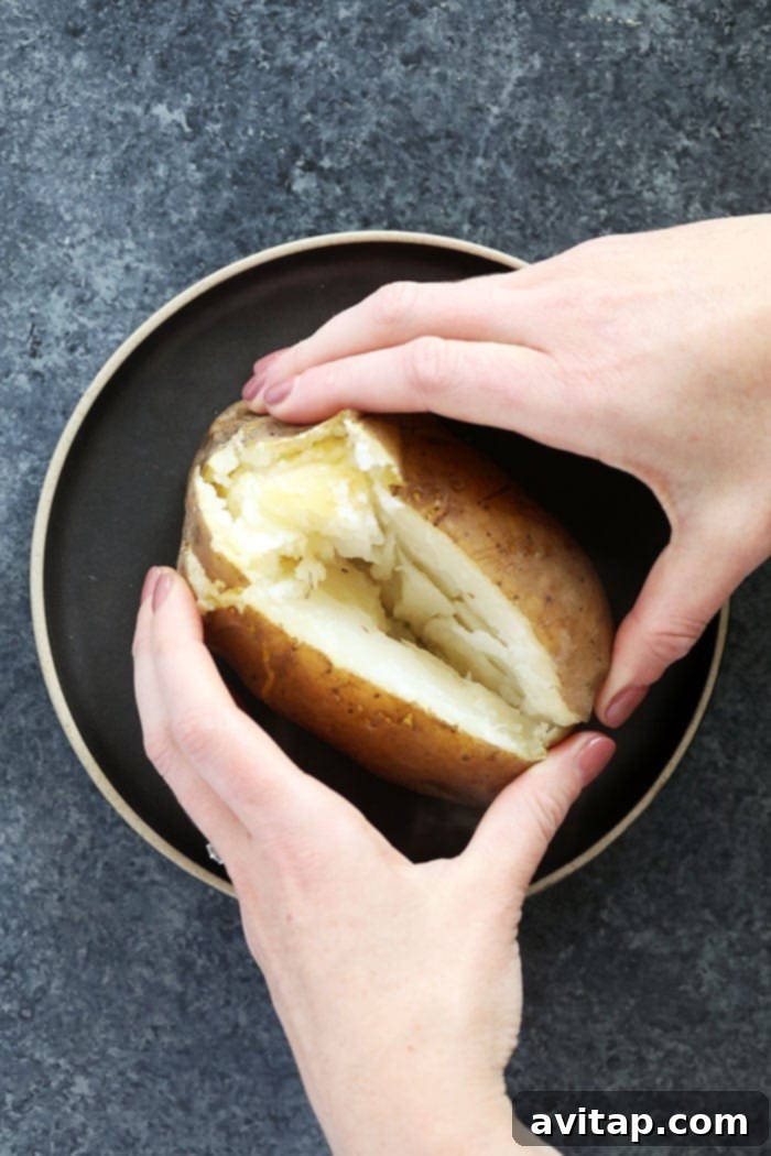 A single crock pot baked potato, sliced open and ready for toppings, on a white plate.
