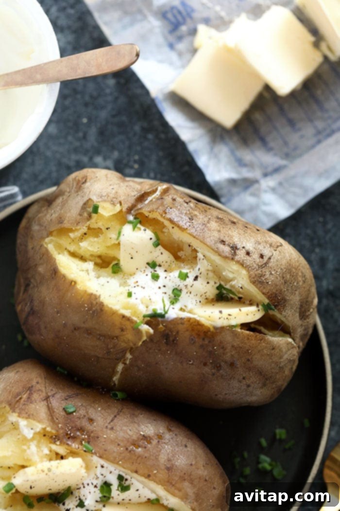 Crock pot baked potatoes topped with sour cream, chives, and a sprinkle of black pepper on a white plate.