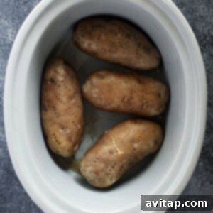 Crock pot baked potatoes served in a white bowl on a gray surface.