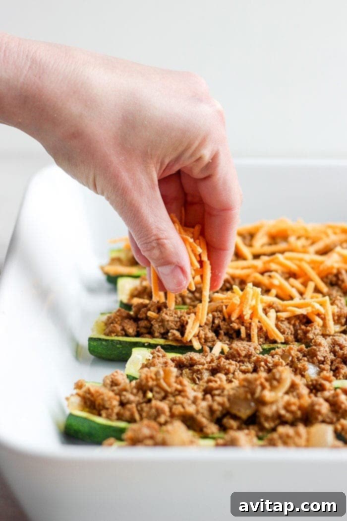 Close-up of shredded cheddar cheese being sprinkled over an assembled Taco Zucchini Boat, ready to be melted.