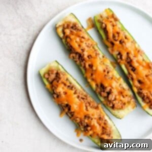 A vibrant, close-up shot of an individual Taco Zucchini Boat, showing the rich filling and melted cheese, on a white background.