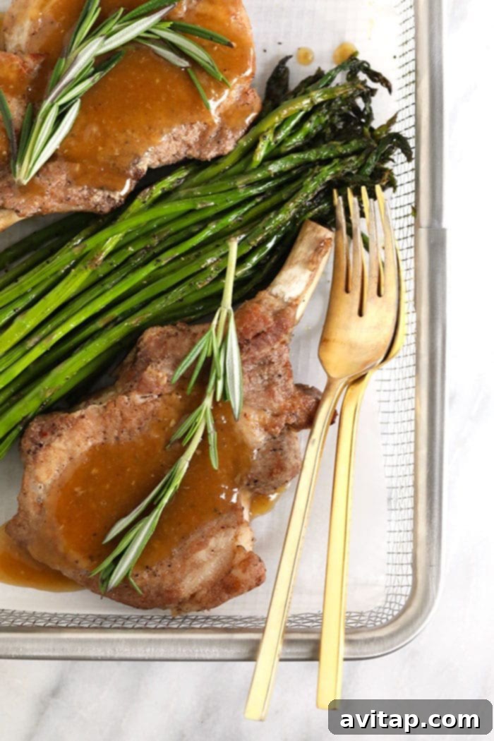 Two juicy Instant Pot pork chops served with asparagus, drizzled with savory whiskey gravy.