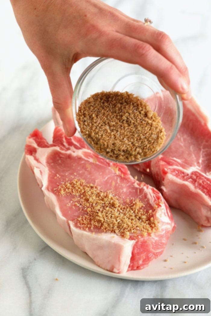 Hand pouring a homemade spice rub over bone-in pork chops on a plate.