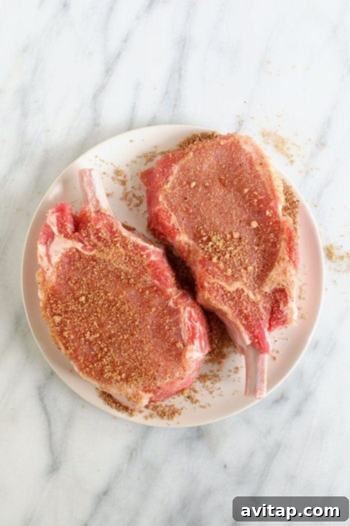 Bone-in pork chops coated generously with a dark, flavorful spice rub, ready for searing.