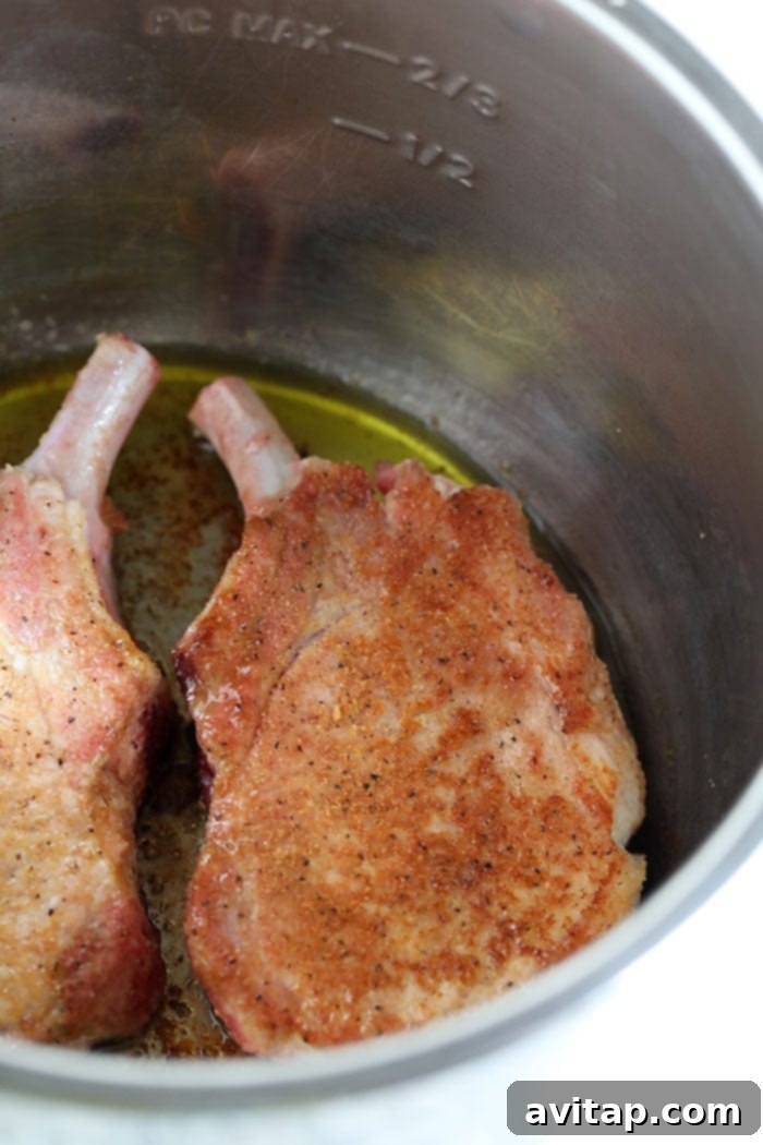 Bone-in pork chops searing in hot olive oil within an Instant Pot, showing a golden-brown crust.