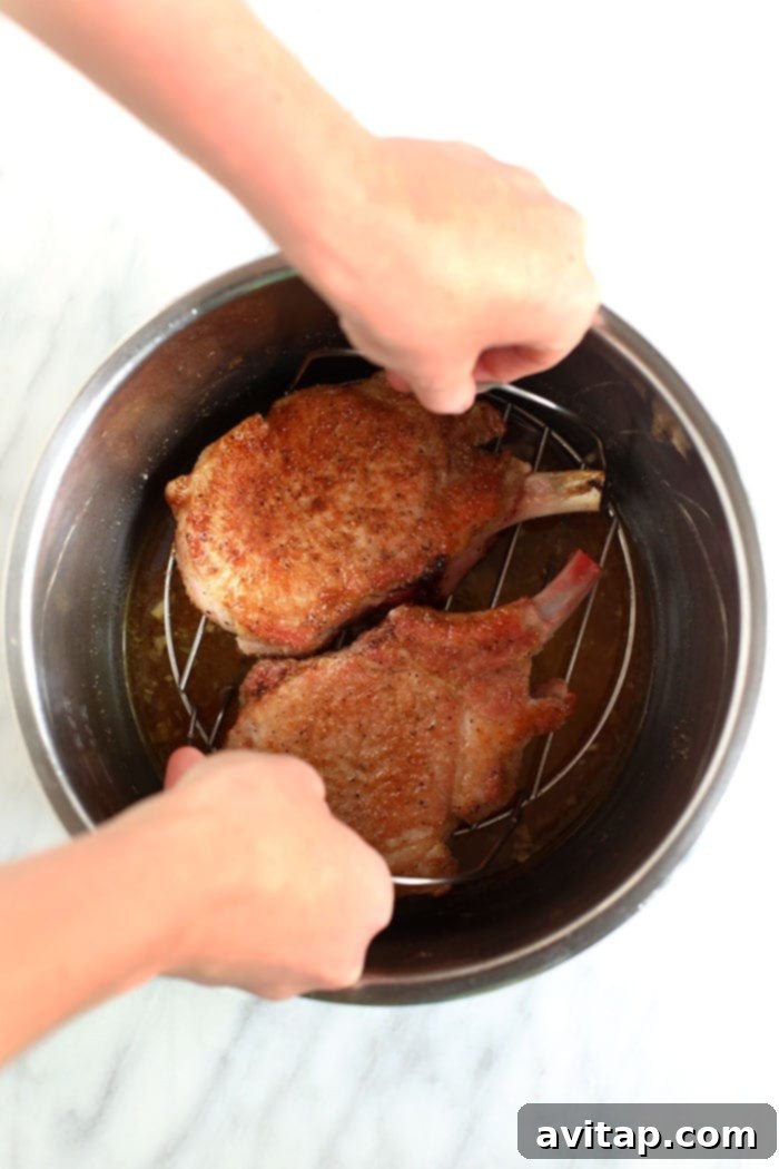 Metal trivet being carefully placed into the Instant Pot over the liquid base, ready for pork chops.