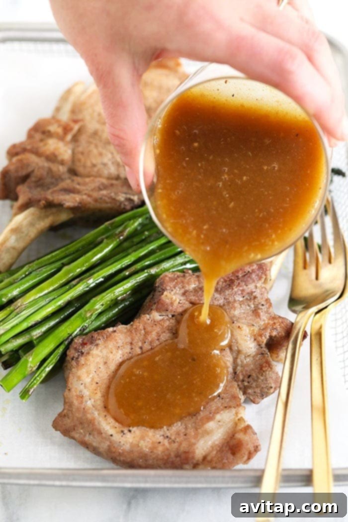 Thick, glossy whiskey gravy being poured generously over a perfectly cooked Instant Pot pork chop.