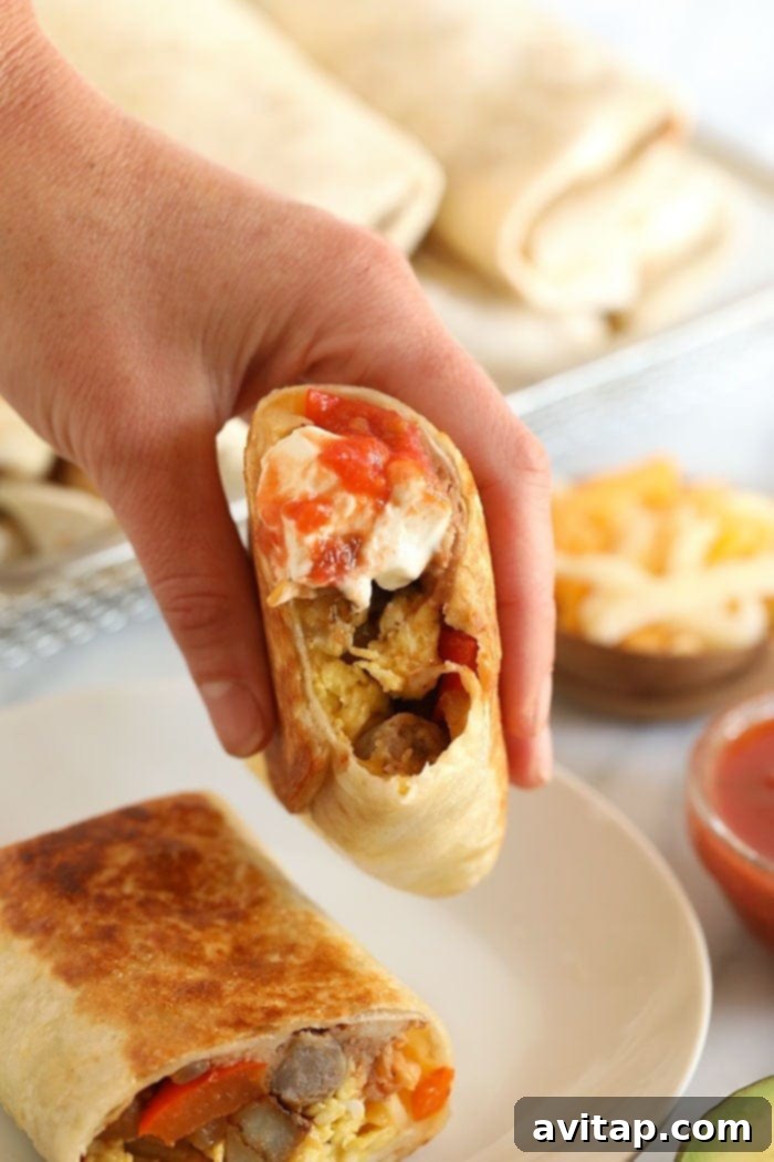 A hand holding two perfectly reheated Fajita Breakfast Burritos, ready for serving.