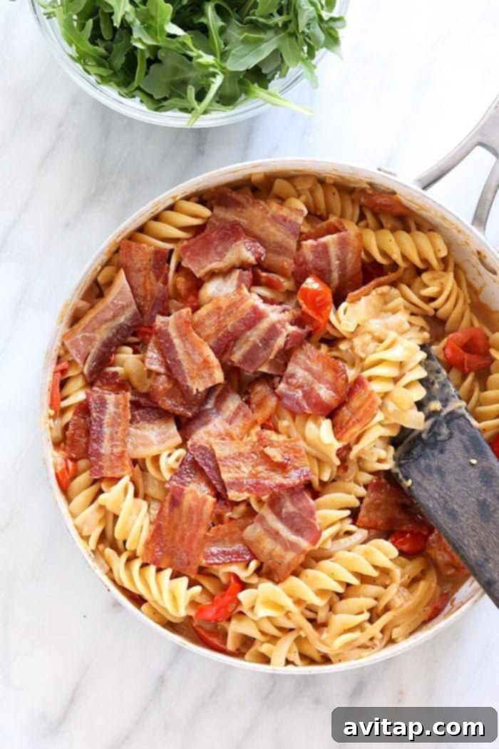 Combining the fresh ingredients for a flavorful BLT pasta dish. Cooked fusilli pasta and chopped crispy bacon being gently tossed into the creamy BLT pasta sauce