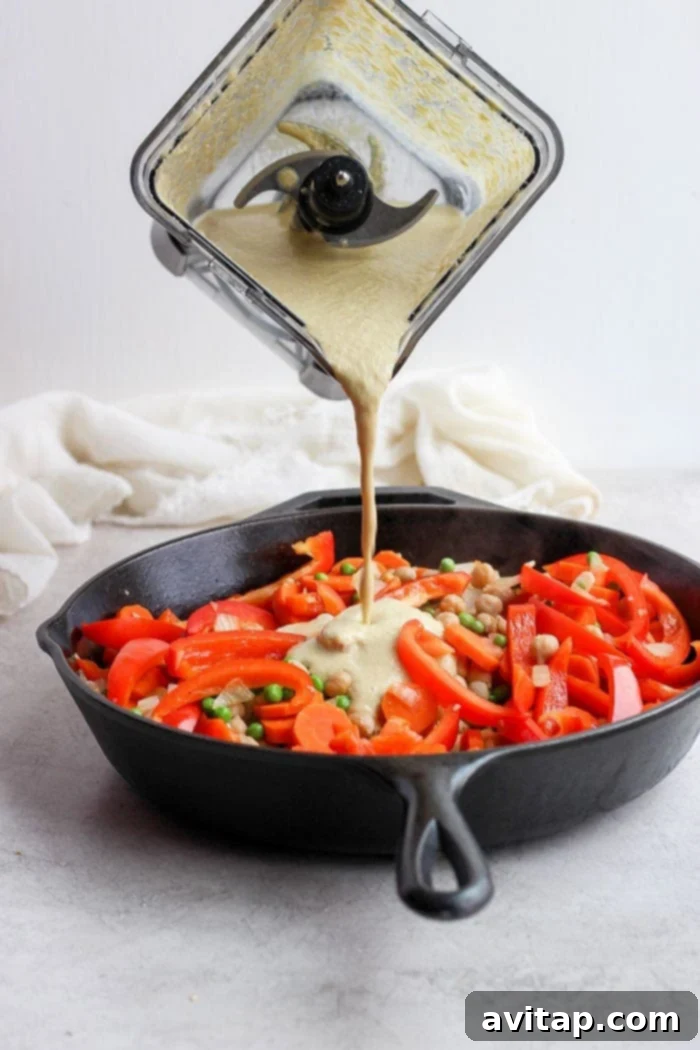 The luscious creamy cashew curry sauce being poured over the sautéed vegetables in a skillet.