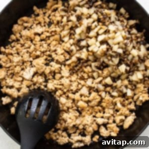 Ground chicken cooking in a skillet, being broken apart with a spatula until fully browned.