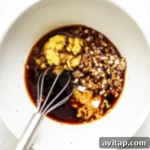 A whisk stirring a rich, dark sauce in a bowl, showing the smooth consistency for the lettuce wraps.