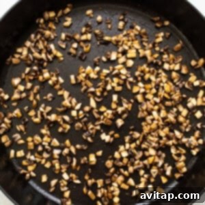 Minced mushrooms sizzling in a hot skillet with sesame oil, releasing their moisture and beginning to brown.