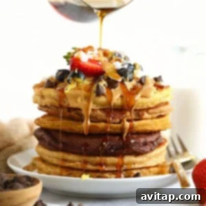 A mouth-watering image of healthy pancakes being drizzled with syrup. A stack of healthy pancakes with syrup being poured over them.