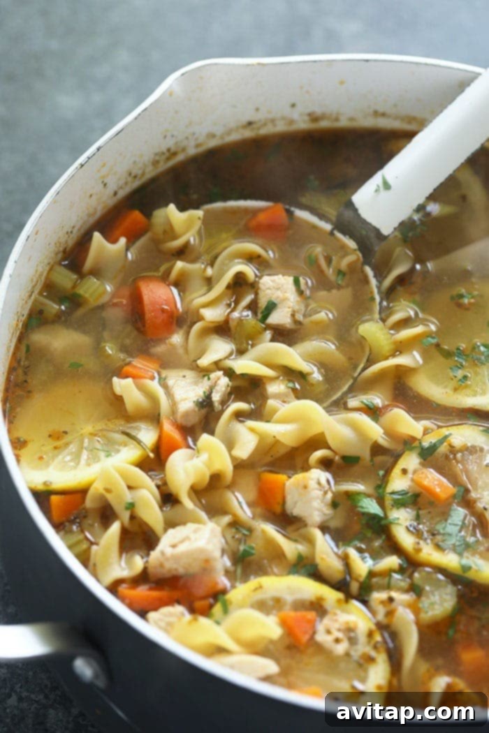 Simmering Homemade Chicken Noodle Soup Large stockpot filled with simmering homemade chicken noodle soup, showing vegetables and chicken.