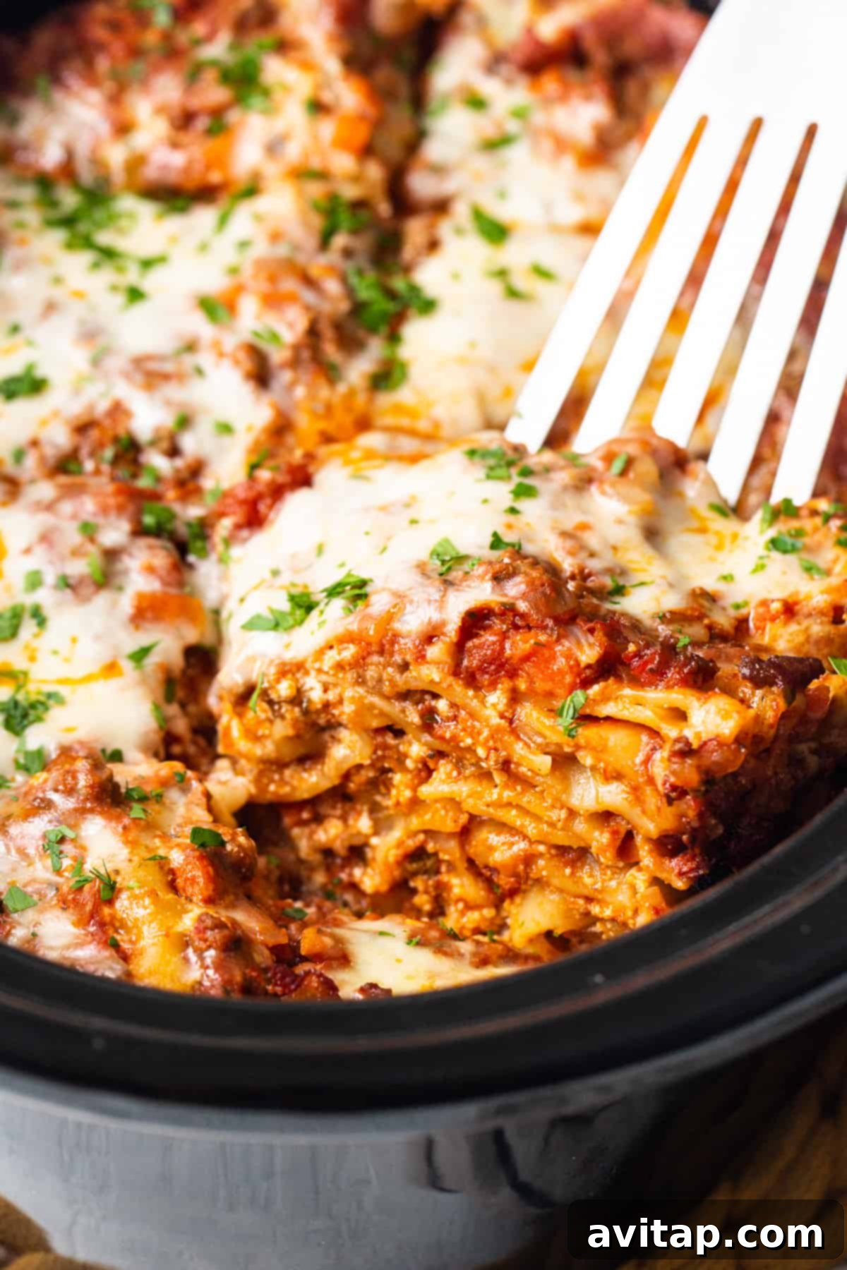 A close-up of a fork digging into a cheesy, rich crockpot lasagna in a casserole dish, steam rising enticingly.