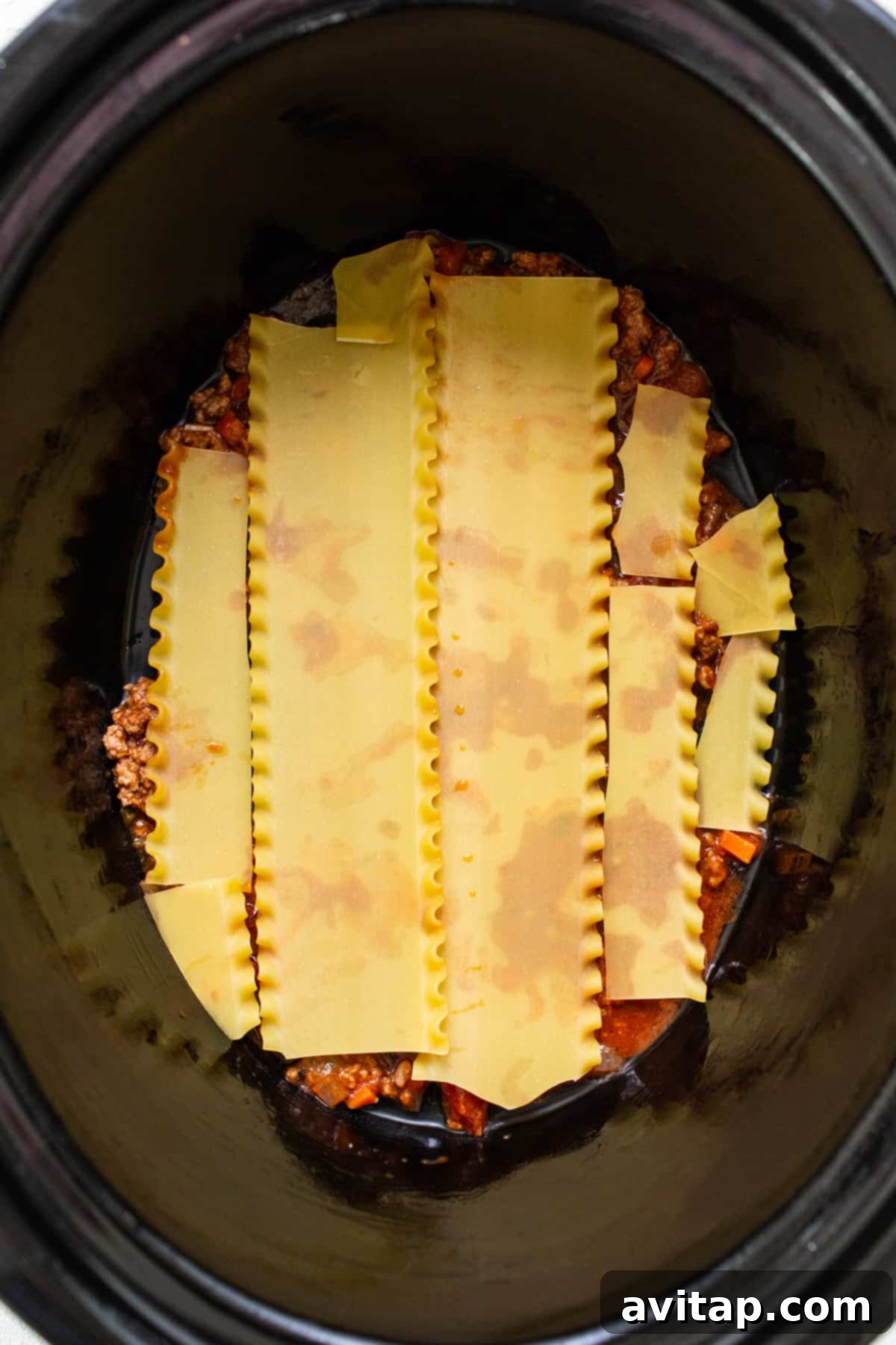 A deep crockpot brimming with layers of pasta, rich red sauce, and bubbling cheese, ready to be served.
