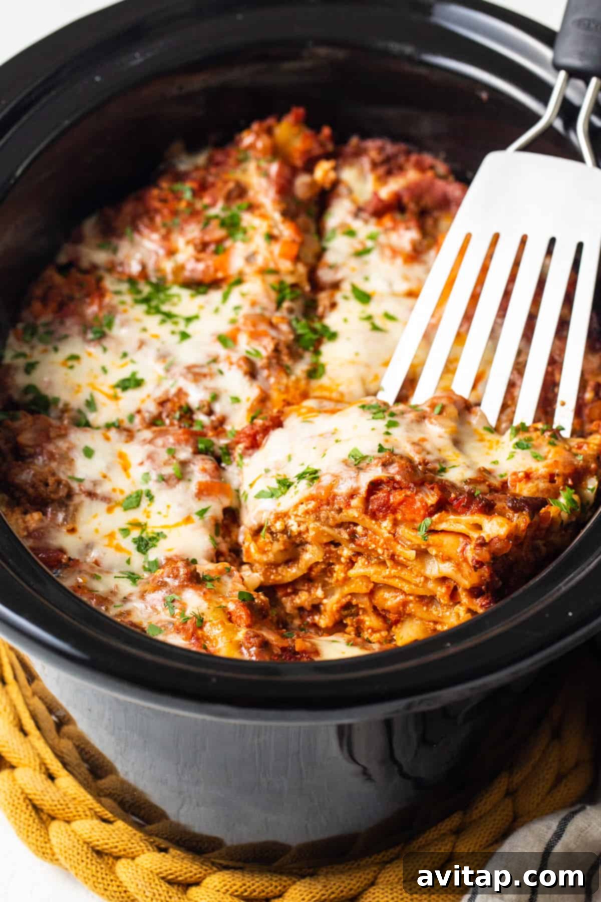 A fork is poised in a generous serving of hot, cheesy lasagna inside a slow cooker, ready to be lifted out.