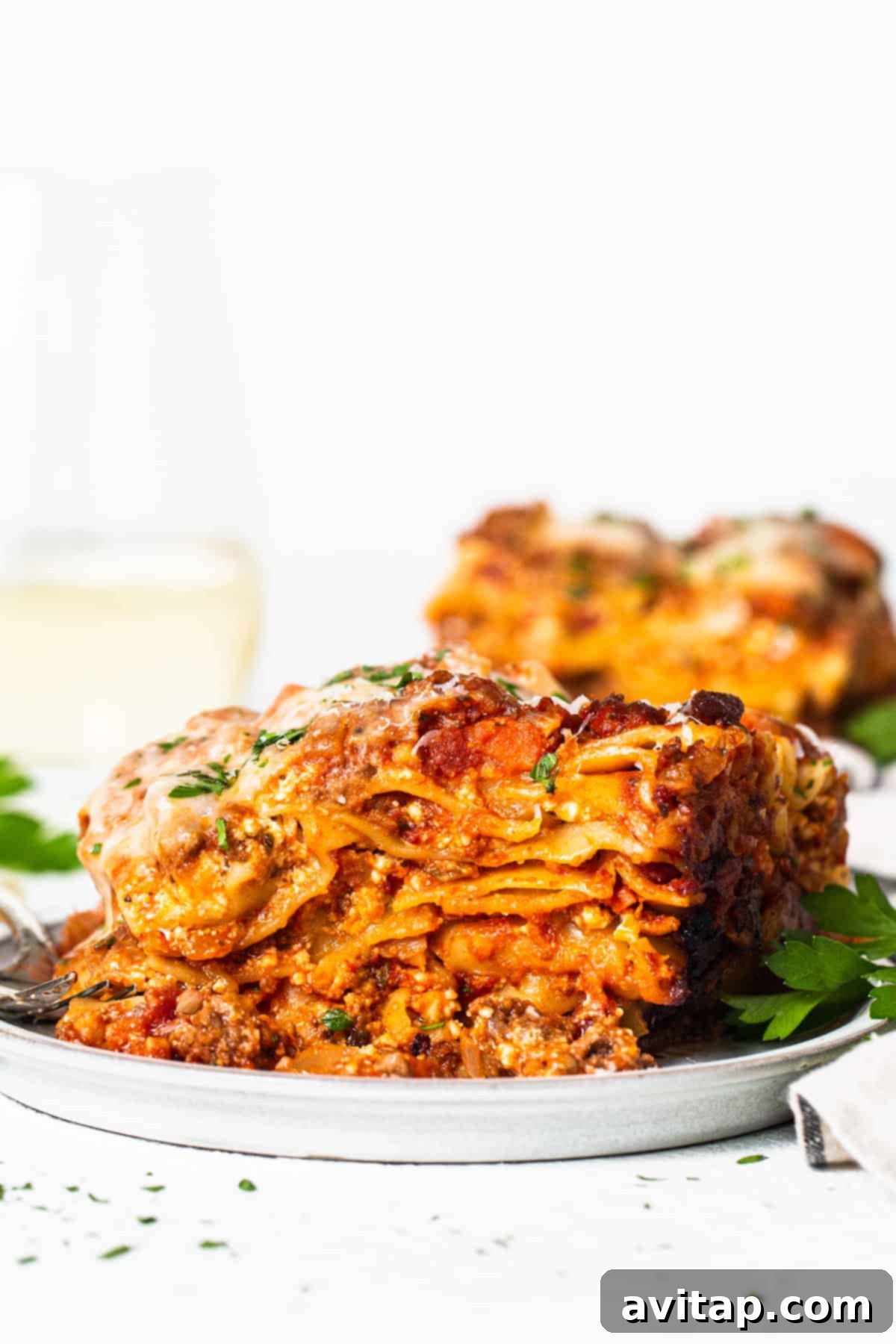 A perfectly plated slice of crockpot lasagna sits on a white plate next to a glass of red wine, ready for a cozy meal.