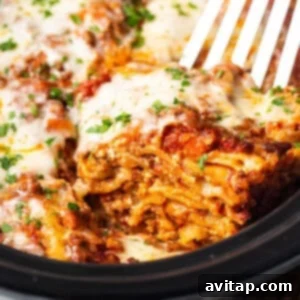 A fork lifts a generous, cheesy portion of crockpot lasagna from the slow cooker.