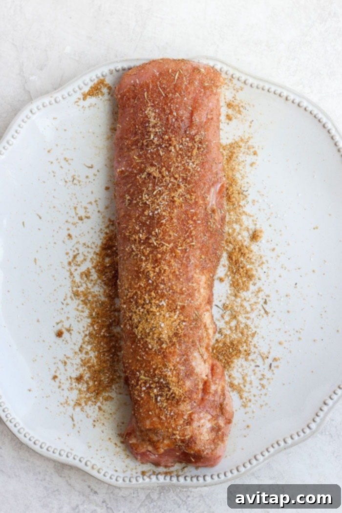 Seasoned pork tenderloin generously coated with a dry rub on a white plate.