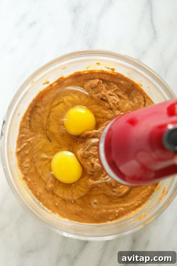 Mixing Pumpkin Cheesecake Filling Pumpkin cheesecake filling being mixed in a bowl with a handheld electric mixer, showing its creamy texture.