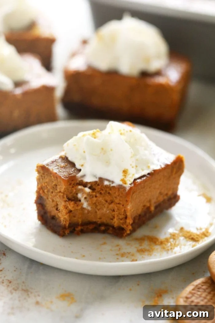 Bitten Pumpkin Cheesecake Bar A pumpkin cheesecake bar with a bite taken out, showing its creamy filling and gingersnap crust, on a white plate.