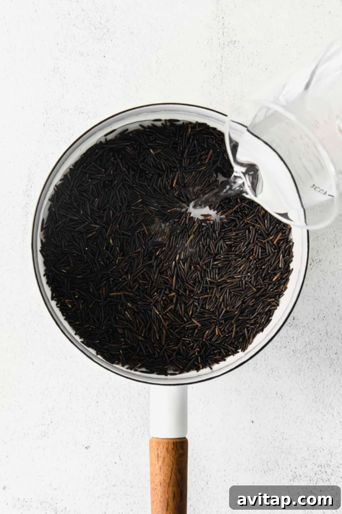 Clear water being carefully poured into a large stock pot filled with dried wild rice grains.