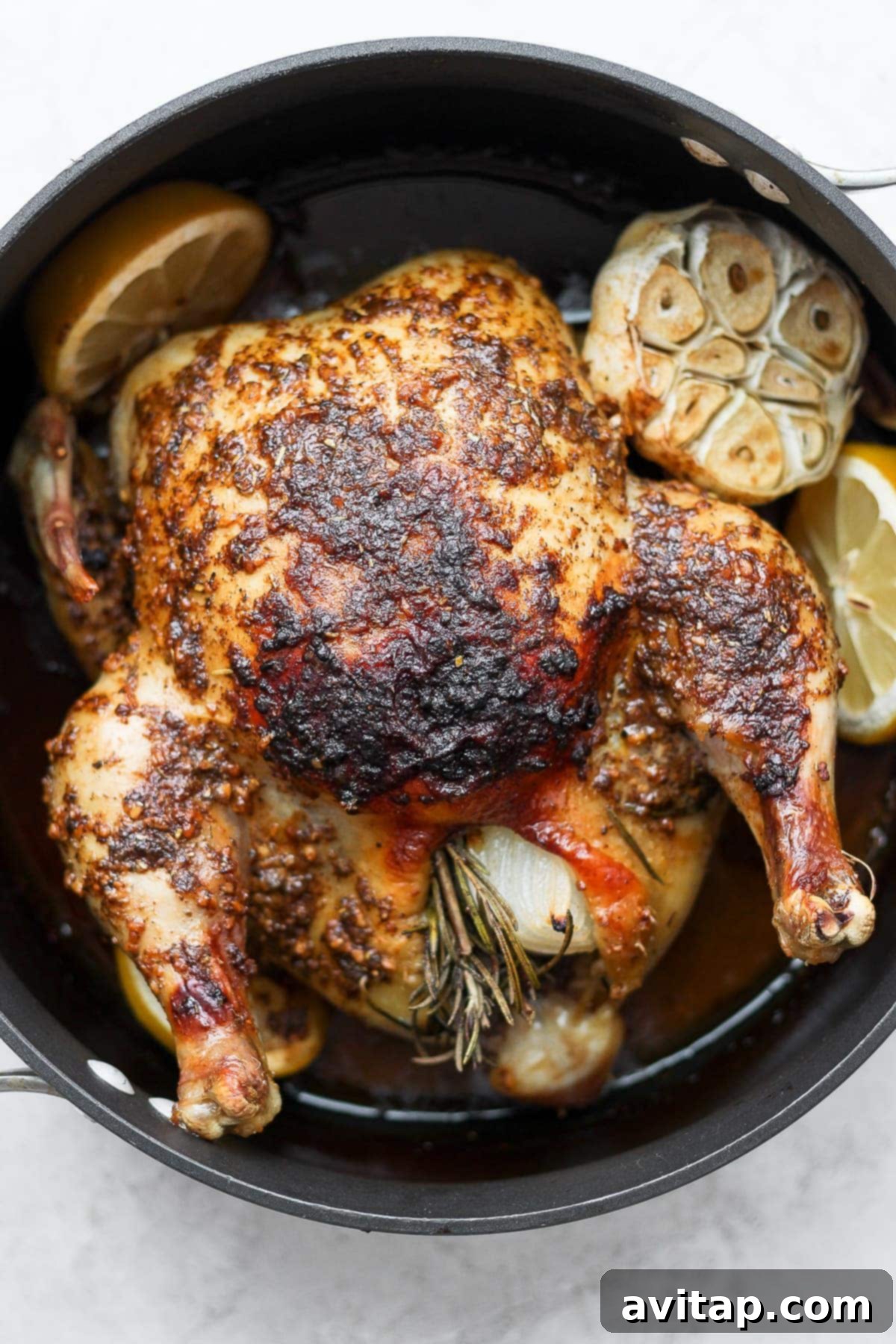 Golden brown whole roasted chicken with garlic and lemon in a roasting pan, ready to be served.
