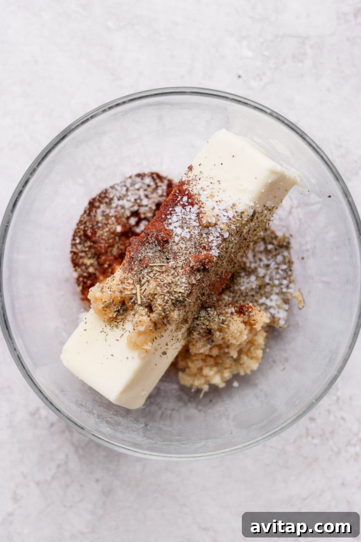 Close-up of a bowl filled with softened butter and a blend of vibrant spices like chili powder and Italian seasoning, ready for application on the chicken.