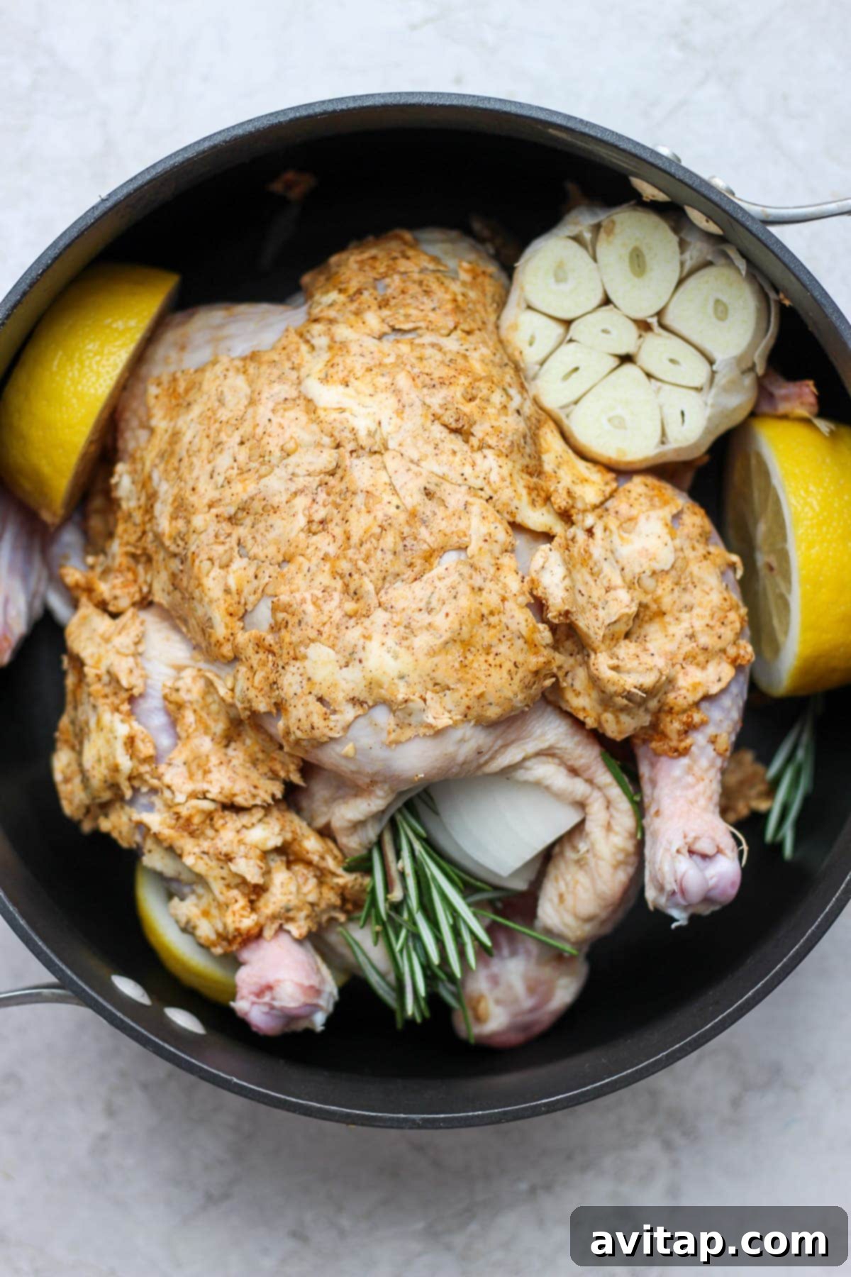 Uncooked whole chicken seasoned and ready in a roasting pan with herbs and lemon slices, prepared for the oven.