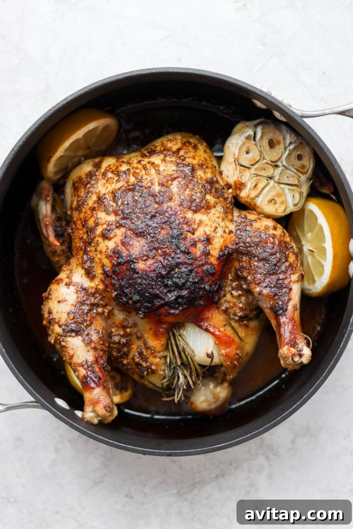 A beautifully roasted whole chicken, golden brown and garnished with fresh herbs, resting in a pan after cooking, ready to be carved.